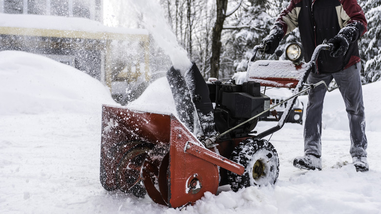 Person in winter clothes uses snow blower to clear his driveway