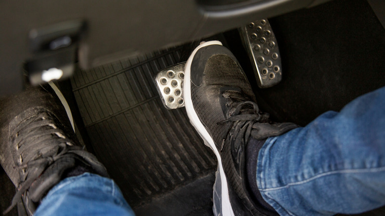 A person in dirty sneakers pressing down on a car's brake pedal