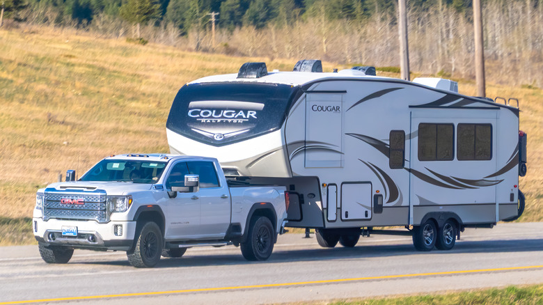 White GMC pickup truck towing a travel trailer on a rural road