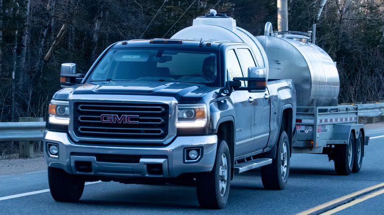 Black GMC pickup truck towing a tanker trailer on a rural road