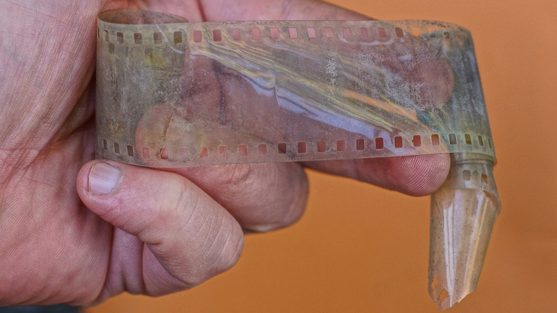 Hand holding old grey film on brown background