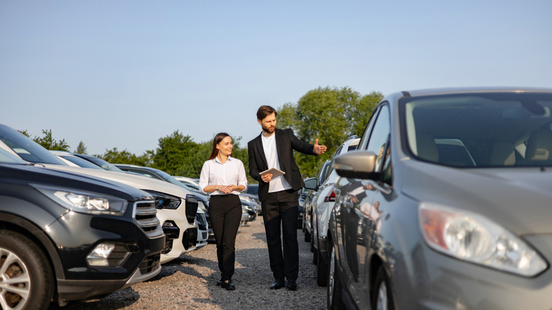 Car salesperson and customer viewing various cars in lot, walking towards camera