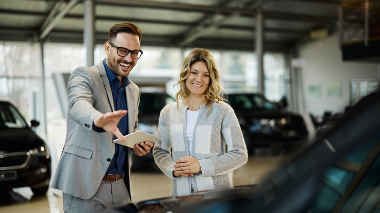 Car salesperson and customer looking at car, salesperson excitedly speaking with hand extended