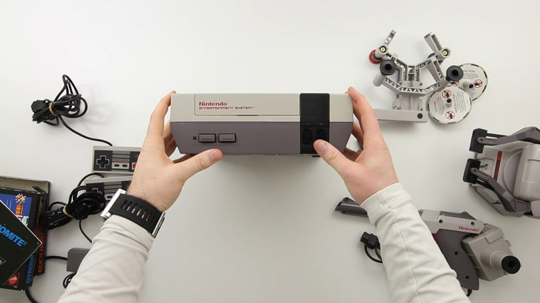 A NES being held surrounded by ROB, zapper, controllers, and duck hunt.