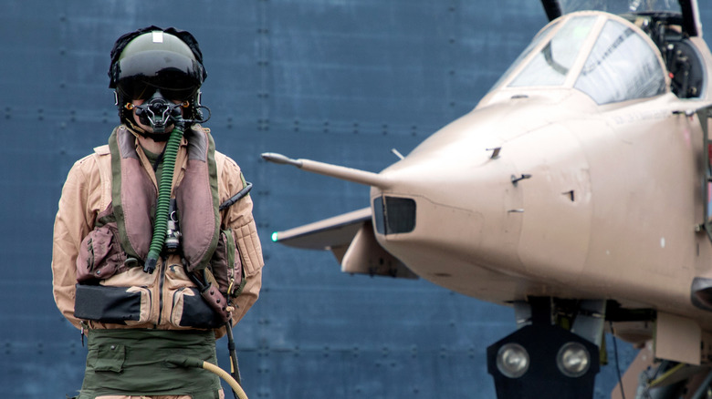 Fighter pilot standing with Military fighter Jet wearing flying helmet, suit and dark visor with oxygen mask
