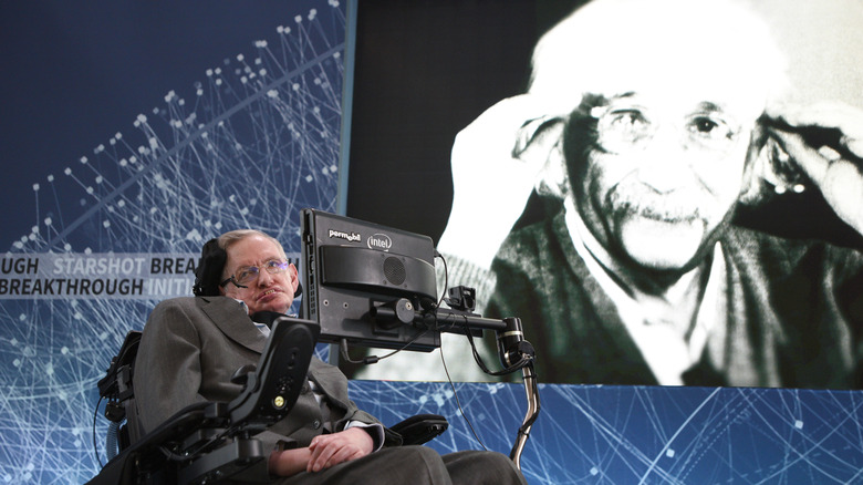 Stephen Hawking in wheelchair on stage with a picture of Albert Einstein behind him