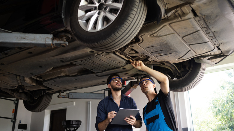 Two men inspect the underside of a car