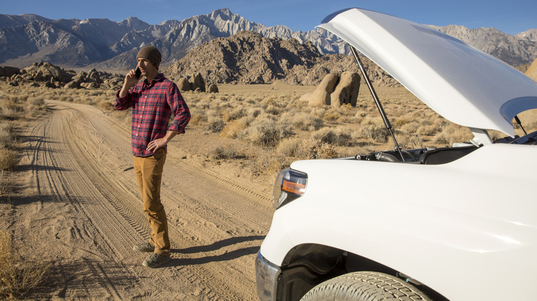 Person calling for help next to a broken-down vehicle in the desert