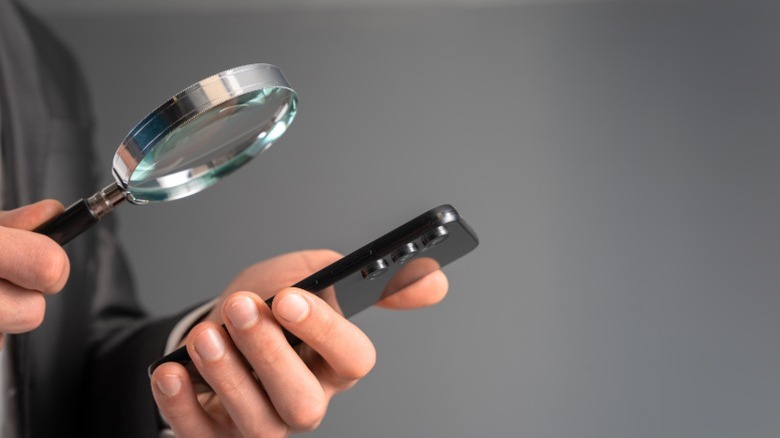 Person inspecting a phone with a magnifying glass