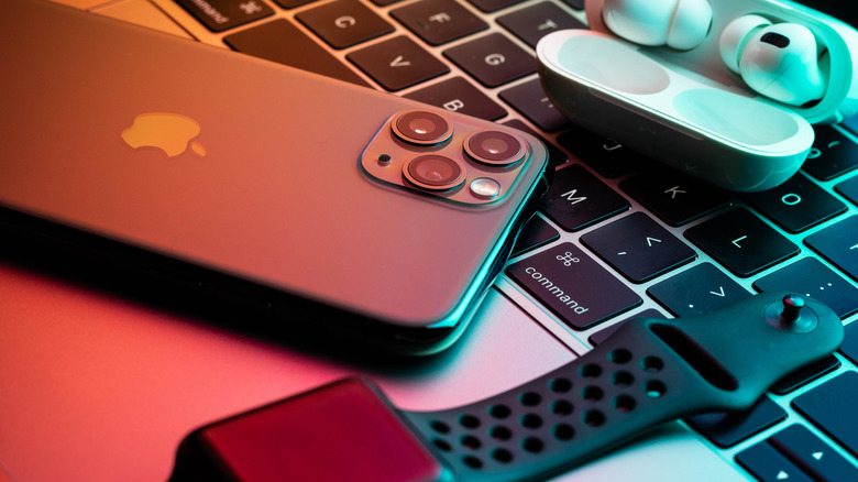 A close up picture of an iphone, airpods, and apple watch, sitting on a macbook keyboard