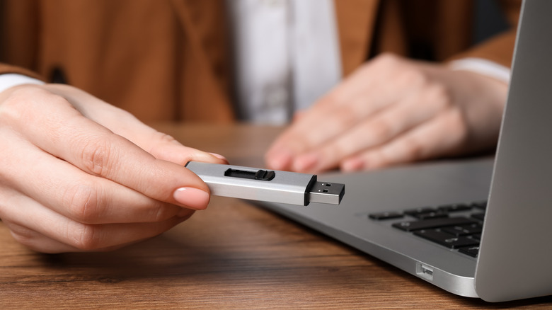 woman holding a USB drive near a laptop