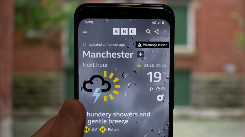 Phone in hand with Weather app open showing percentage of rain