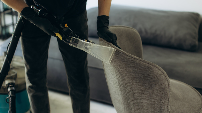A man using a carpet cleaner's upholstery attachment to clean a chair