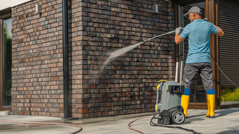 man using pressure washer on wall