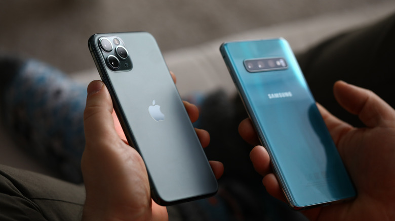 Male hand hold Apple iPhone Pro and Samsung Galaxy S10.