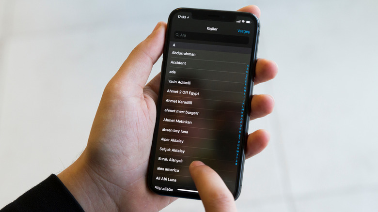 A person holding an iPhone with contacts list open
