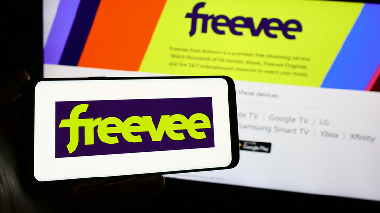 A person holding a smartphone with the Freevee logo on it.