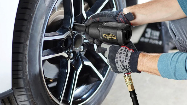 Mechanic in gloves using air impact wrench on wheel lugs