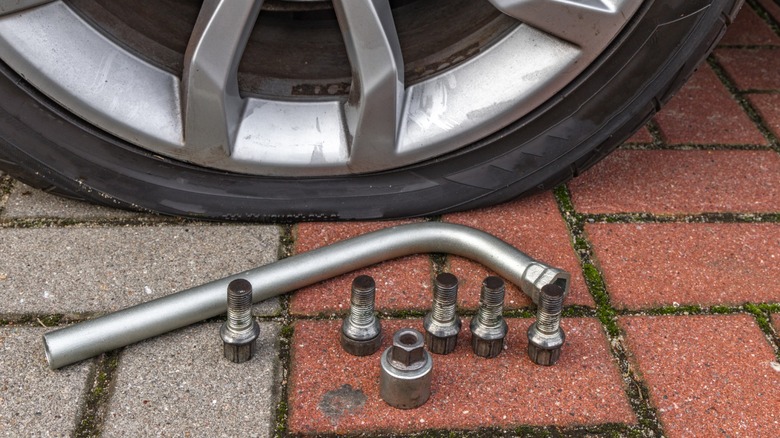Five wheel bolts on the floor next to a torque rench and a flat tire wheel