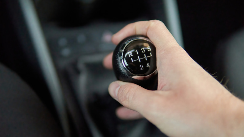 Hand holding Manual gearbox transmission gear shifter knob handle stick shift in the car interior.