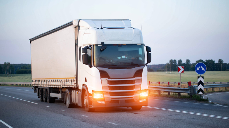 A modern truck with headlights on and a tilted semi-trailer transports cargo in the evening.
