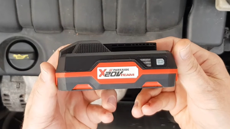 Side view of a 20V power drill battery over a car engine bay