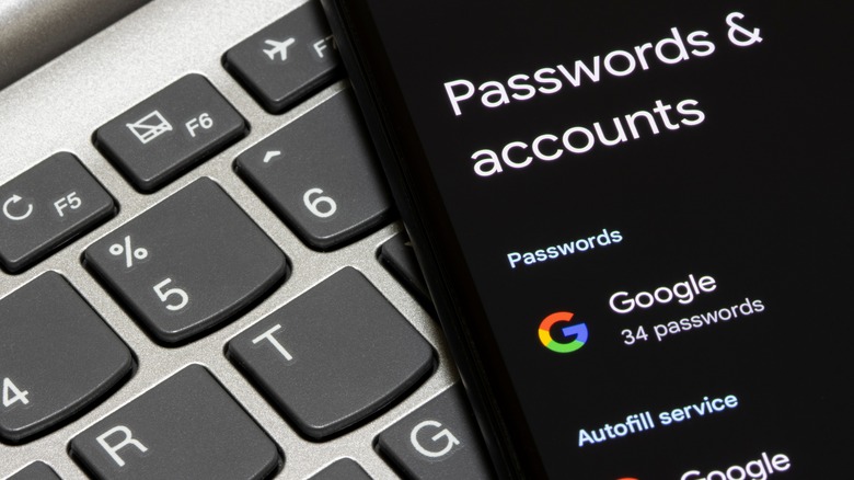 Google Passwords & accounts screen on a smartphone with computer keyboard in background.