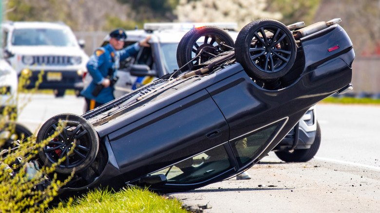 Car accident with overturned car, police officer, and police vehicle in background