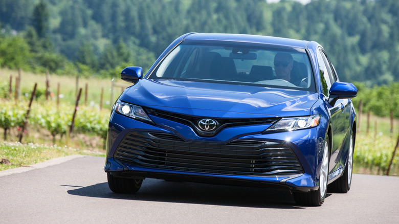 Front view of a blue 2018 Toyota Camry driving on country road.