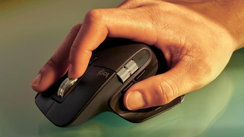 A person's hand holding a Logitech MX Master 3S mouse on a glass surface