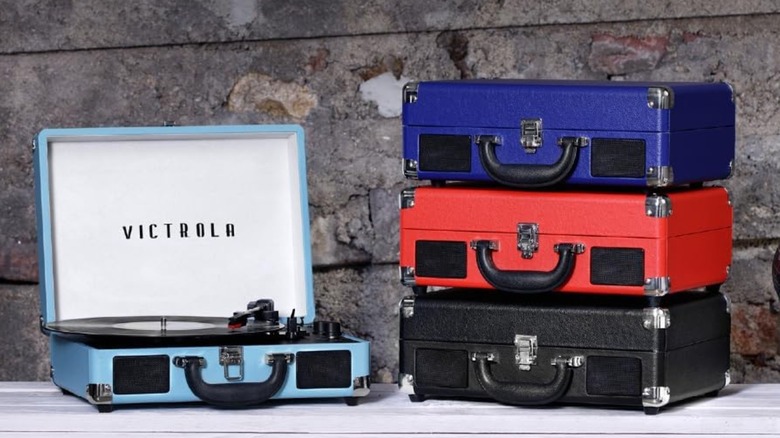 An open Victrola Journey record player suitcase next to stacked suitcases of different colors