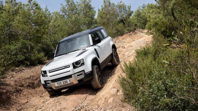 A white Land Rover Defender 110 driving down a steep off-road trail