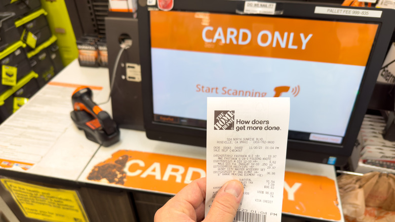 Holding paper receipt next to a Card Only self check out register inside Home Depot