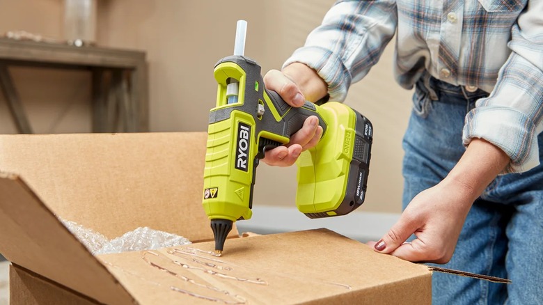 A person applying hot glue to a carboard box.