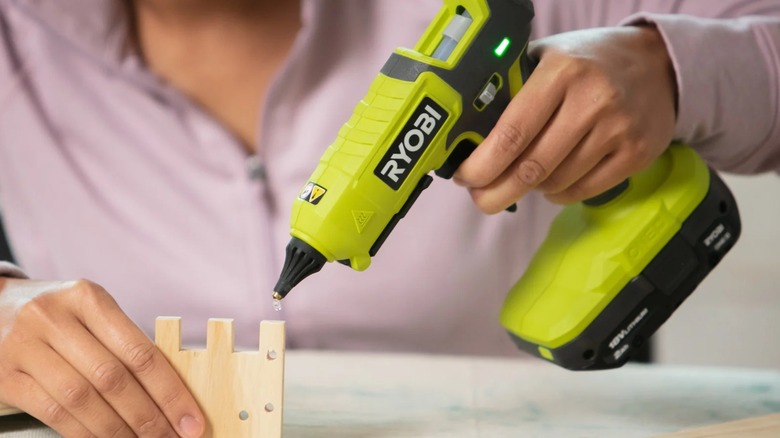 A person using a Ryobi glue gun on wood.