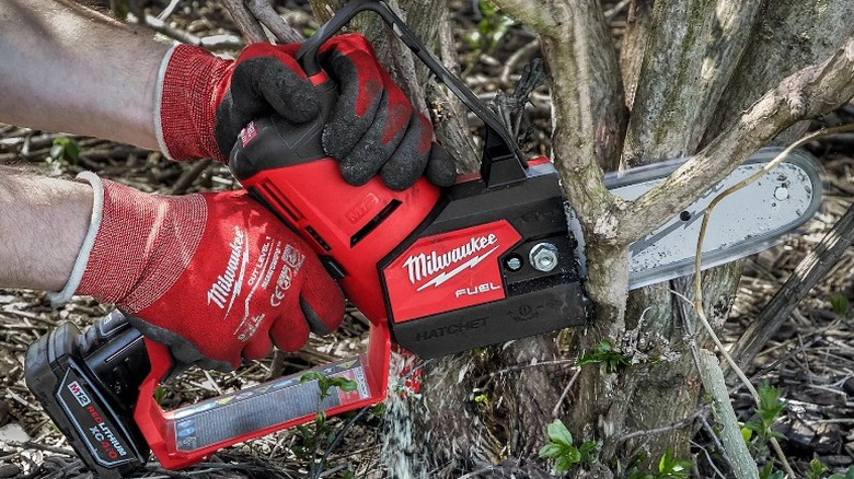 Person cutting branch with Milwaukee M12 Fuel 6-inch Brushless Pruning Hatchet Mini Chainsaw