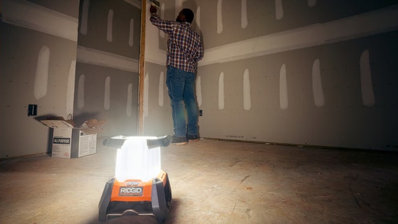 Ridgid 18V Cordless 360° Area Light in the ground while a man paints in the background