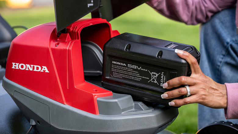 User placing an 8Ah battery into a Honda mower