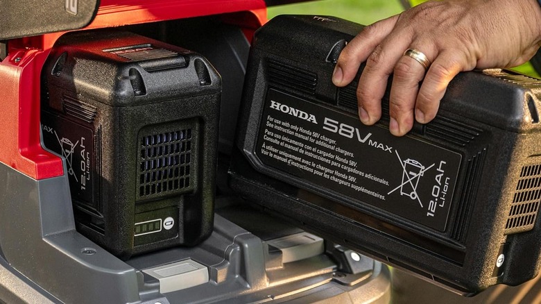 A person adding a battery one-handed to Honda's HRX-BE electric mower