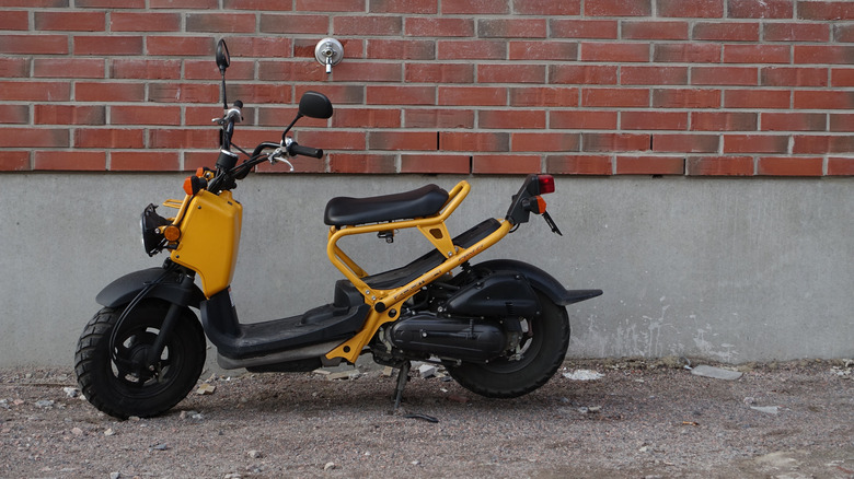 Side view of a Honda Ruckus in yellow against a brick wall