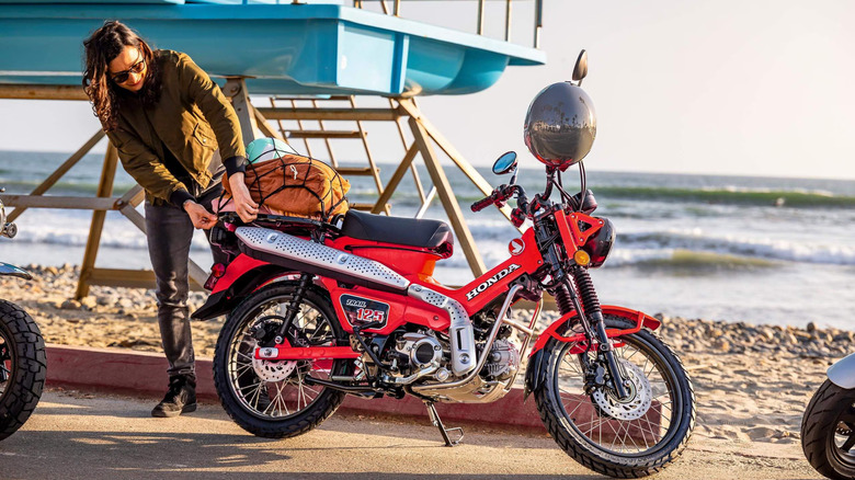 A person standing beside a red Honda Trail125 mini motorcycle
