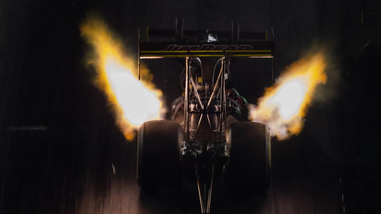 Top fuel dragster launching at night, rear-view