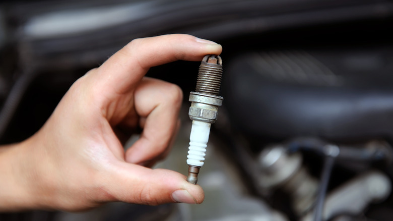 A person holding a spark plug, with an out of focus engine in the background