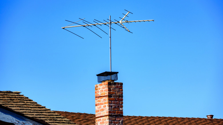 A traditional TV antenna mounted alongside a brick chimney on a shingled roof