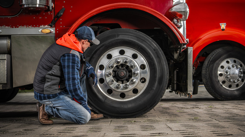 Person inspecting the tires on an unidentified red semi truck