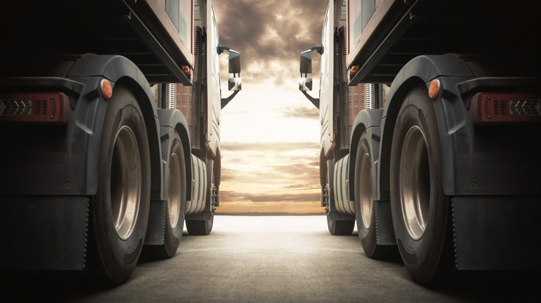 A low angle shot of two European semi trucks next to each other, cloudy sunset in the background