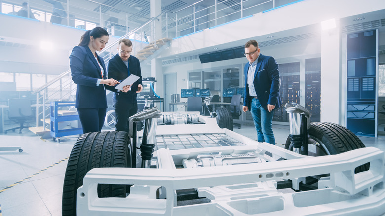 Automotive engineers looking at an EV chassis and consulting a tablet