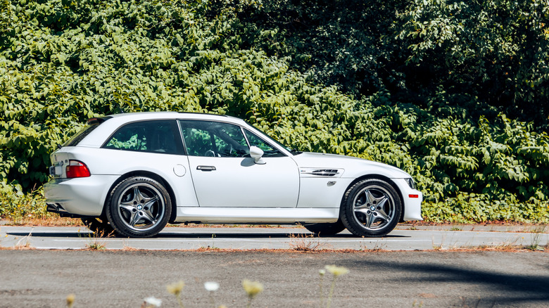 Side profile of white BMW Z3 M Roadster parked in front of trees.