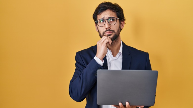 Man wearing a suit holding laptop and thinking