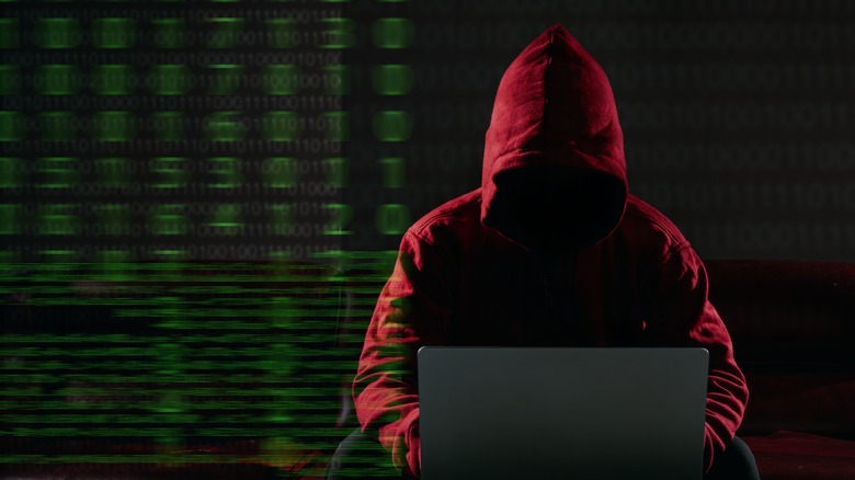 A hacker in red hoodie working on a laptop